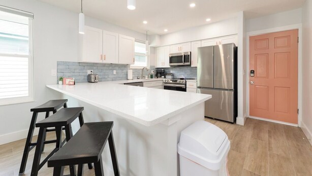 A modern kitchen with white cabinetry, stainless steel appliances, and a central island with stools. - Be A Nomad | 2BR Upper Unit | 2 Blocks to Neptune Beach (Neptune Beach)