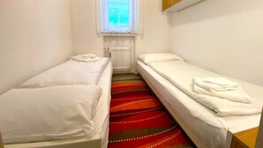Ein kleines, sauberes Zimmer mit zwei Einzelbetten, einem Fenster mit Vorhängen und einer Heizung.
