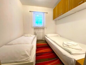 A small, clean room with two single beds, a window with curtains, and a radiator. - Salute 108 # 4-bed apartment, Dusche, WC 4-Bettwohnung, Dusche, WC by Interhome (Leukerbad)
