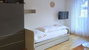 A bedroom with a bed, a wardrobe, a television, and a window with curtains. - Leuca 24 # 2-bed apartment, Dusche, WC 2-Bettwohnung, Dusche, WC by Interhome (Leukerbad)