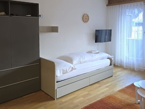 A bedroom with a bed, a wardrobe, a television, and a window with curtains. - Leuca 24 # 2-bed apartment, Dusche, WC 2-Bettwohnung, Dusche, WC by Interhome (Leukerbad)