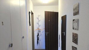 A hallway with a white door, a wooden door, and a coat rack with a coat and umbrella. - Leuca 24 # 2-bed apartment, Dusche, WC 2-Bettwohnung, Dusche, WC by Interhome (Leukerbad)