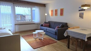 A furnished room with a sofa, a small table, a coffee table, and a window with curtains. - Leuca 24 # 2-bed apartment, Dusche, WC 2-Bettwohnung, Dusche, WC by Interhome (Leukerbad)