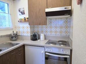 Cocina compacta con lavavajillas, estufa con hervidor y ventana con vista a ovejas.