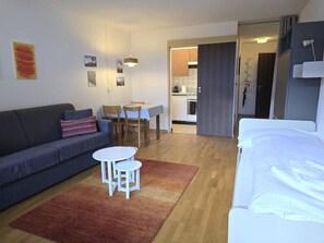 A compact living space with a sofa, a small dining table, a kitchen area, and a bed. - Leuca 24 # 2-bed apartment, Dusche, WC 2-Bettwohnung, Dusche, WC by Interhome (Leukerbad)