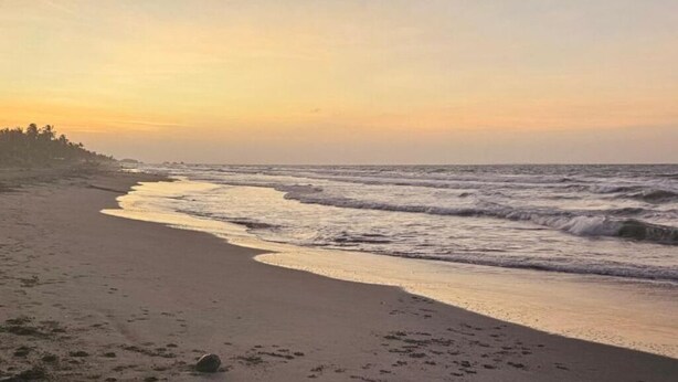 A beach with waves, a clear sky, and a distant shoreline.