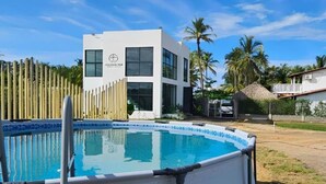 A modern building with a pool, surrounded by palm trees and a wooden fence.
