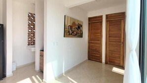 A hallway with a tiled floor, a wooden door, a wall-mounted artwork, and a decorative wall panel.