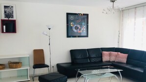 Ett modernt vardagsrum med en svart lädersoffa, ett soffbord i glas, en golvlampa och en inramad abstrakt målning på väggen.