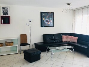 A modern living room with a black leather sofa, a glass coffee table, a floor lamp, and a framed abstract painting on the wall. - Edelweiss C 11 # 4-bed apartment, Dusche und Bad, WC by Interhome (Leukerbad)