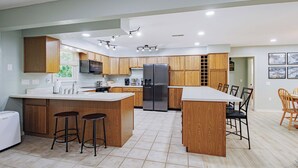 Uma cozinha moderna com armários de madeira, uma ilha central com banquetas, uma geladeira e uma área de refeições com cadeiras.