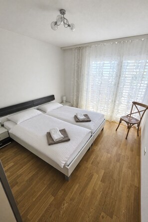 A hotel room with two beds, a wooden floor, a chair, and a ceiling light fixture. - Ambassador B22 # 2-bed apartment, Dusche, WC 2-Bettwohnung, Dusche, WC by Interhome (Leukerbad)