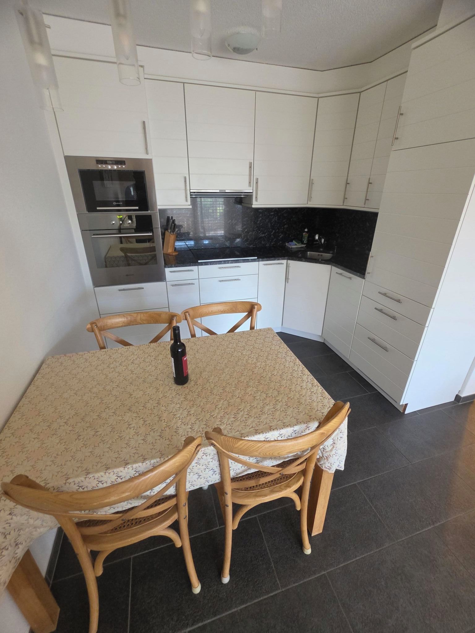 A compact kitchen with white cabinets, a black countertop, and a dining table with chairs.