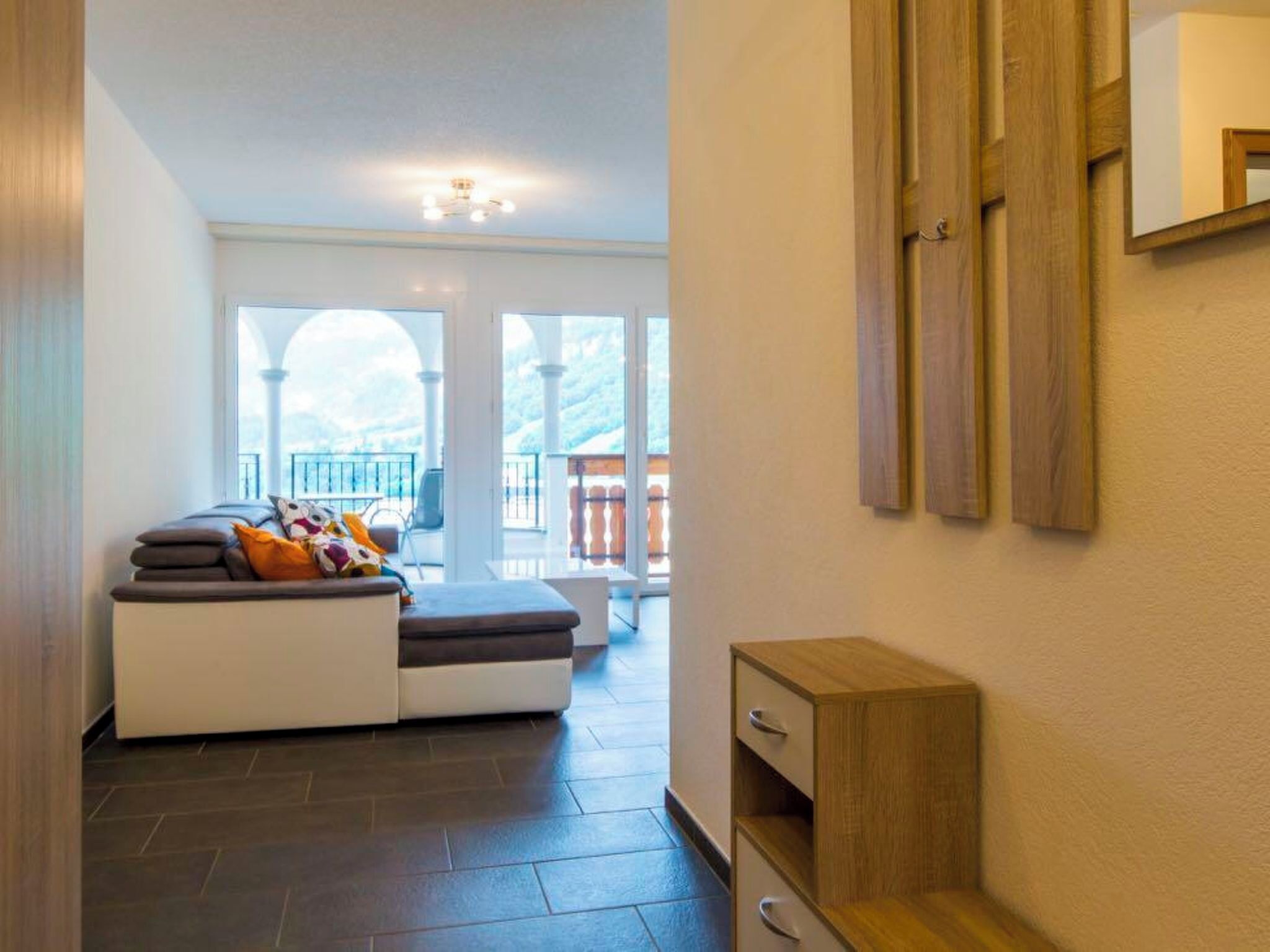 Ein modernes Interieur mit einer Sofagarnitur, einem Holzschrank und Blick auf einen Balkon.