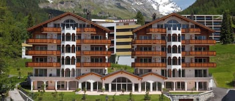 Un hôtel à plusieurs étages, doté de balcons, d’une façade en pierre et surplombant un paysage montagneux.