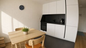 A compact kitchen with a dining table, chairs, a clock, and a potted plant. - Residenz Belair Leukerbad # 2-bed apartment, Dusche, WC by Interhome (Leukerbad)