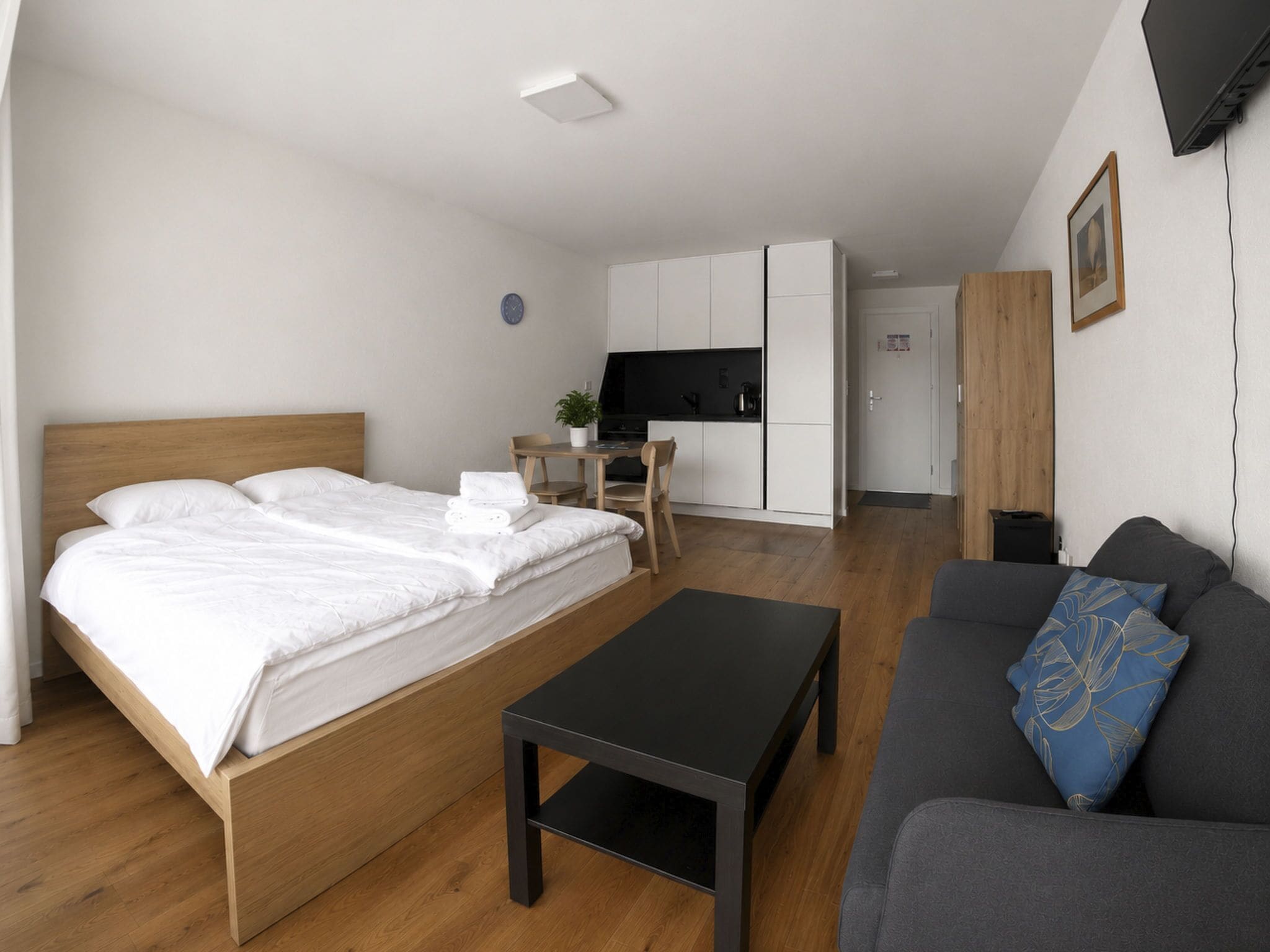 Ein modernes Hotelzimmer mit Bett, einer Couch, einem kleinen Tisch, einer Küchenzeile und einem Fernseher.