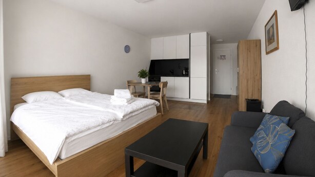 A modern hotel room with a bed, a sofa, a small table, a kitchenette, and a television. - Residenz Belair Leukerbad # 2-bed apartment, Dusche, WC by Interhome (Leukerbad)
