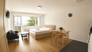 A bedroom with a bed, a desk, a chair, a TV, and a view of mountains through a window. - Residenz Belair Leukerbad # 2-bed apartment, Dusche, WC by Interhome (Leukerbad)
