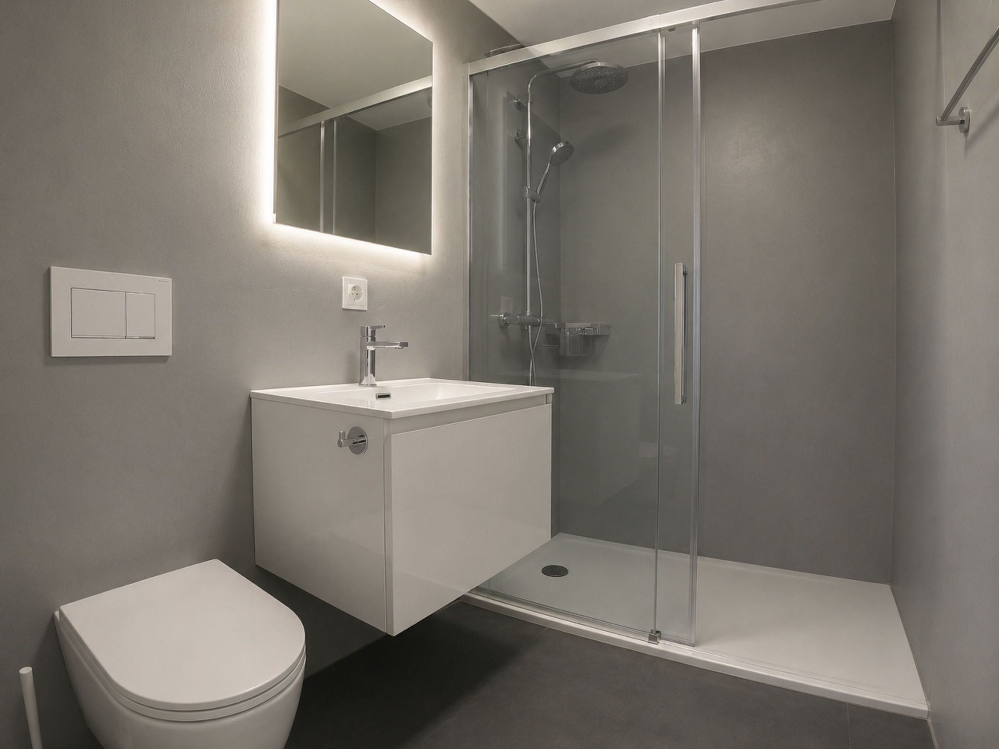 Ein modernes Badezimmer mit einer gläsernen Duschkabine, einem weißen Waschbecken und einer Toilette.
