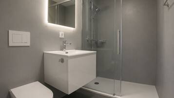 Ein modernes Badezimmer mit einer gläsernen Duschkabine, einem weißen Waschbecken und einer Toilette.