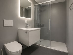 Ein modernes Badezimmer mit einer gläsernen Duschkabine, einem weißen Waschbecken und einer Toilette.