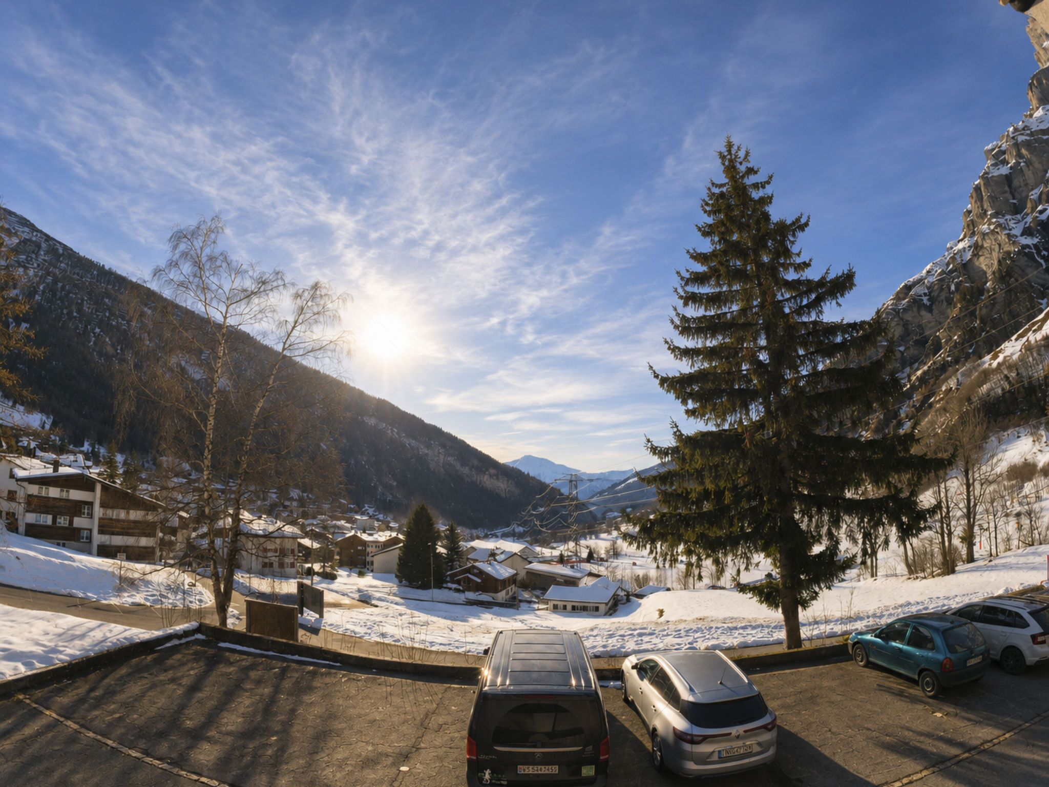 Ein Parkplatz mit Autos, Bergen im Hintergrund und blauem Himmel.