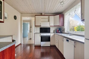 A kitchen with a stove, oven, and dishwasher, wooden flooring, and a window with a view. - Perfect 3-bedroom house in charming Rødbyhavn for your getaway (Rødbyhavn)