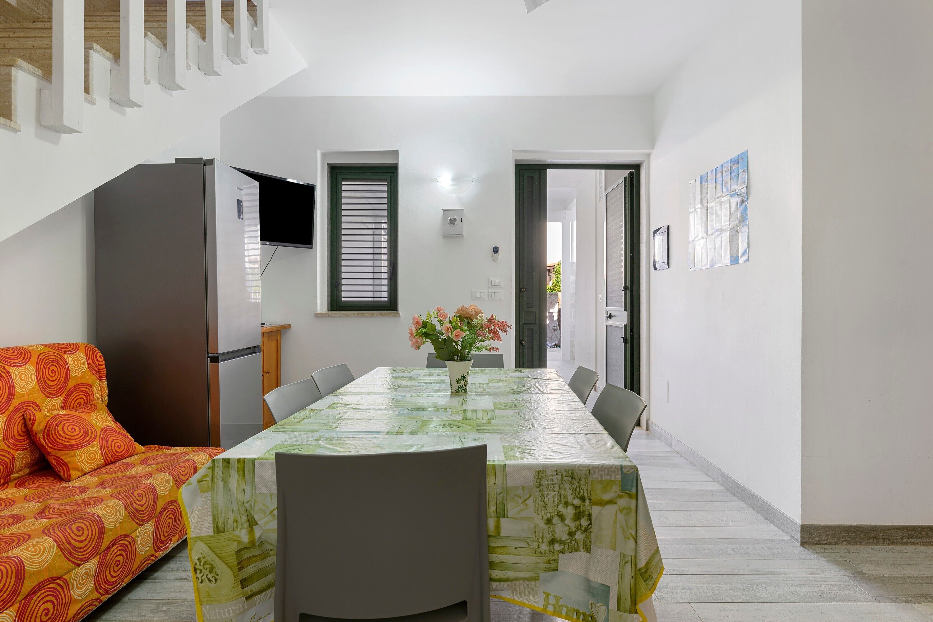 A dining area with a table, chairs, a sofa, a TV, and a door leading to another room.