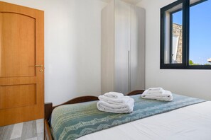 A bedroom with a bed, a wooden door, a wardrobe, and a window.