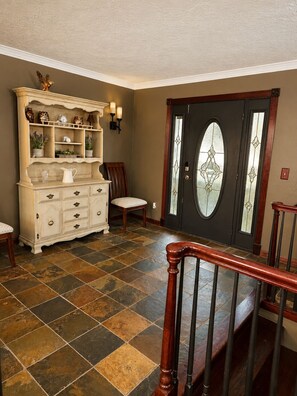 A foyer with a dark wooden door, a white console table with decorative items, and a staircase with a wooden railing. - 3 bed 2 bath in Kennesaw with Game Room Near KSU and Truist Park (Kennesaw)