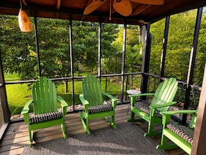A covered porch with green Adirondack chairs and a small table, surrounded by a wooden deck and a metal fence. - 3 bed 2 bath in Kennesaw with Game Room Near KSU and Truist Park (Kennesaw)