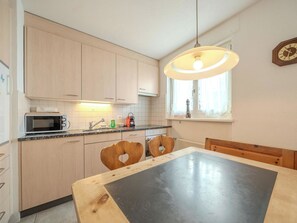 A kitchen with wooden cabinets, a microwave, a sink, and a table with heart-shaped chairs. - Viktoria A22 by Arosa Vacations Appartement/Fewo, Dusche und Badewanne, 3 Schlaf by Interhome (Arosa)