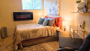 Ein Schlafzimmer mit Bett, Fernseher, Fenster, Lampe und Stuhl.