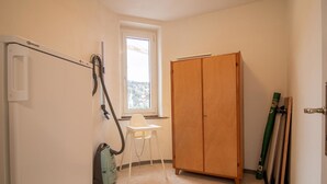 Una habitación con un armario de madera, un aspirador, una ventana y una silla.