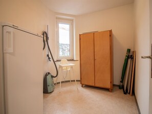Ein Zimmer mit Holzschrank, Staubsauger, Fenster und Stuhl.