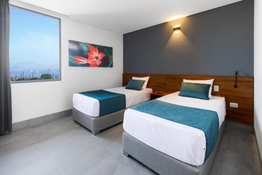 Une chambre d’hôtel avec deux lits, une grande fenêtre, un tableau et un luminaire fixé au mur.