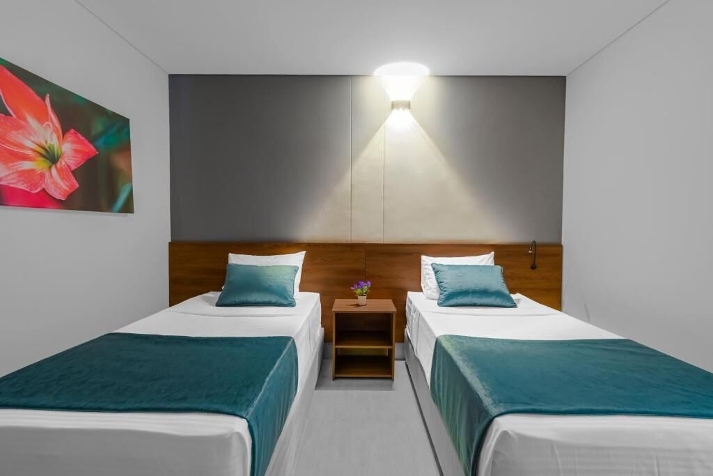 A hotel room with two beds, a nightstand, a wall-mounted light, and a painting.