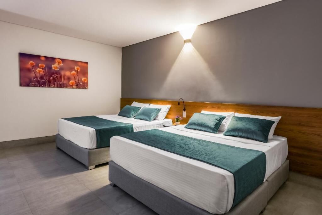 Habitación de hotel con dos camas, un cuadro en la pared y una lámpara fijada a la pared.