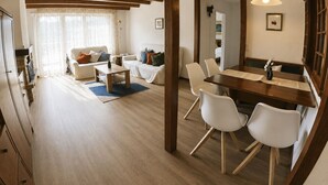 Un'ampia zona giorno con soffitto in legno, un tavolo da pranzo con sedie e una cucina visibile attraverso un'apertura.