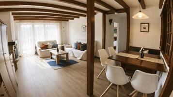 Un salón amplio con techo de madera, una mesa de comedor con sillas, y una cocina visible a través de un vano abierto.