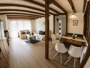 A spacious living area with a wooden ceiling, a dining table with chairs, and a kitchen area visible through an open doorway. - Residenz Clabina Leukerbad # 6-bed apartment, Bad, WC by Interhome (Leukerbad)