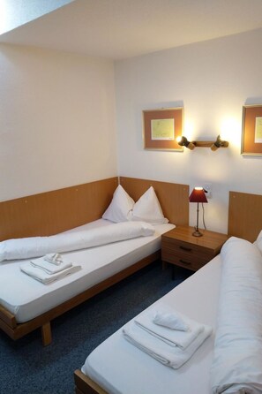 A hotel room with two single beds, a wooden headboard, a nightstand with a lamp, and wall-mounted light fixtures. - Fortuna 317 # 6-bed apartment, Dusche, WC 6-Bettwohnung, Dusche, WC by Interhome (Leukerbad)