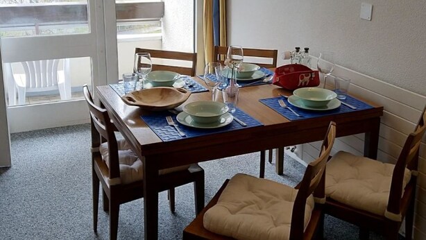 Un coin repas avec une table dressée pour quatre personnes, des chaises, une fenêtre avec des rideaux et un luminaire fixé au mur.
