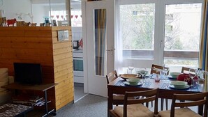 Un coin repas avec une table dressée pour quatre personnes, un téléviseur dans un coin et une vue sur l’extérieur par une fenêtre.