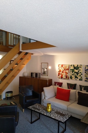 A living room with a staircase, a sofa set, a coffee table, and wall art. - Fortuna 317 # 6-bed apartment, Dusche, WC 6-Bettwohnung, Dusche, WC by Interhome (Leukerbad)