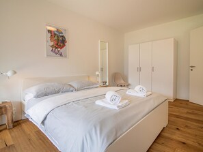 Ett sovrum med en säng, två sängbord, ett litet bord, en garderob, en spegel och ett konstverk som hänger på väggen.