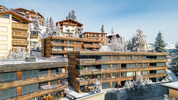 Un hôtel à plusieurs étages, doté de balcons, d’une façade en bois et entouré d’un paysage enneigé.