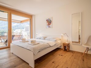 A bedroom with a bed, a bedside table, a lamp, a chair, a large window, and a painting. - PlantA rosa by Arosa Holiday Appartement/Fewo, Dusche oder Bad, WC, 6-Bettwohnun by Interhome (Arosa)