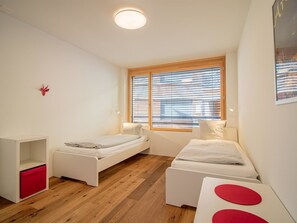 A modern bedroom with two single beds, a wooden floor, a window with blinds, and a small red decoration on the wall. - PlantA rosa by Arosa Holiday Appartement/Fewo, Dusche oder Bad, WC, 6-Bettwohnun by Interhome (Arosa)